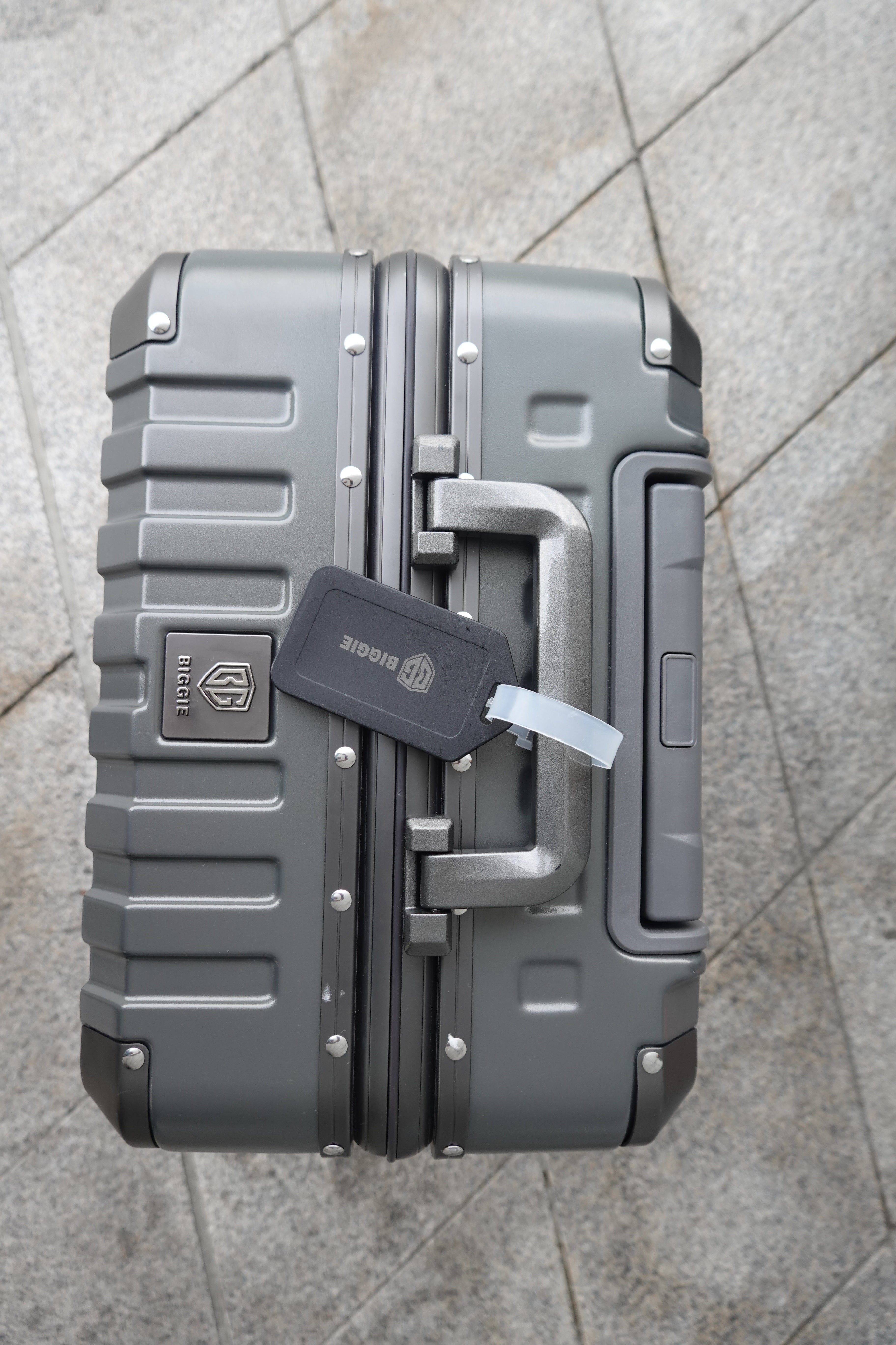 Gray hard-shell suitcase with a visible brand logo on a tiled floor.