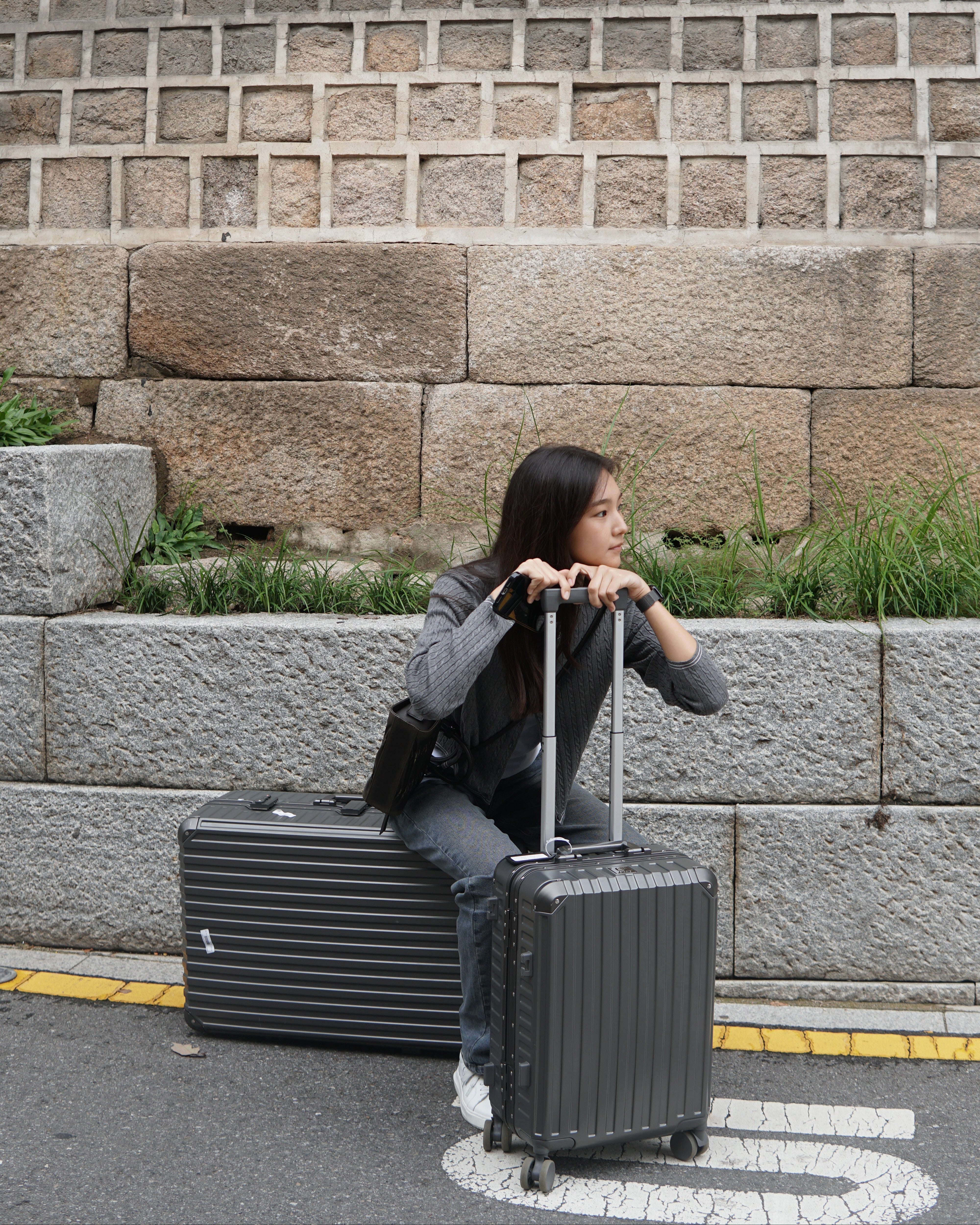 Person with suitcases on a street next to a stone wall